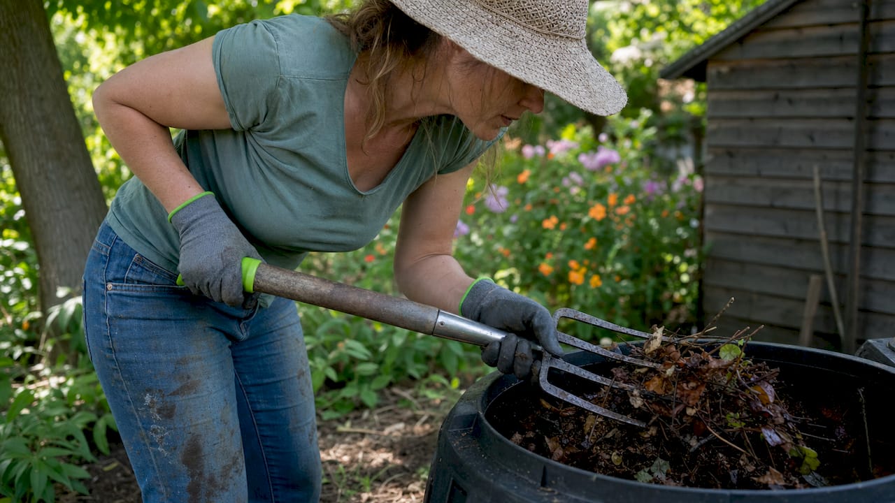 Woman turning compost pile in backyard